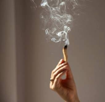 Hand holding a lit smudge stick, smoke rising