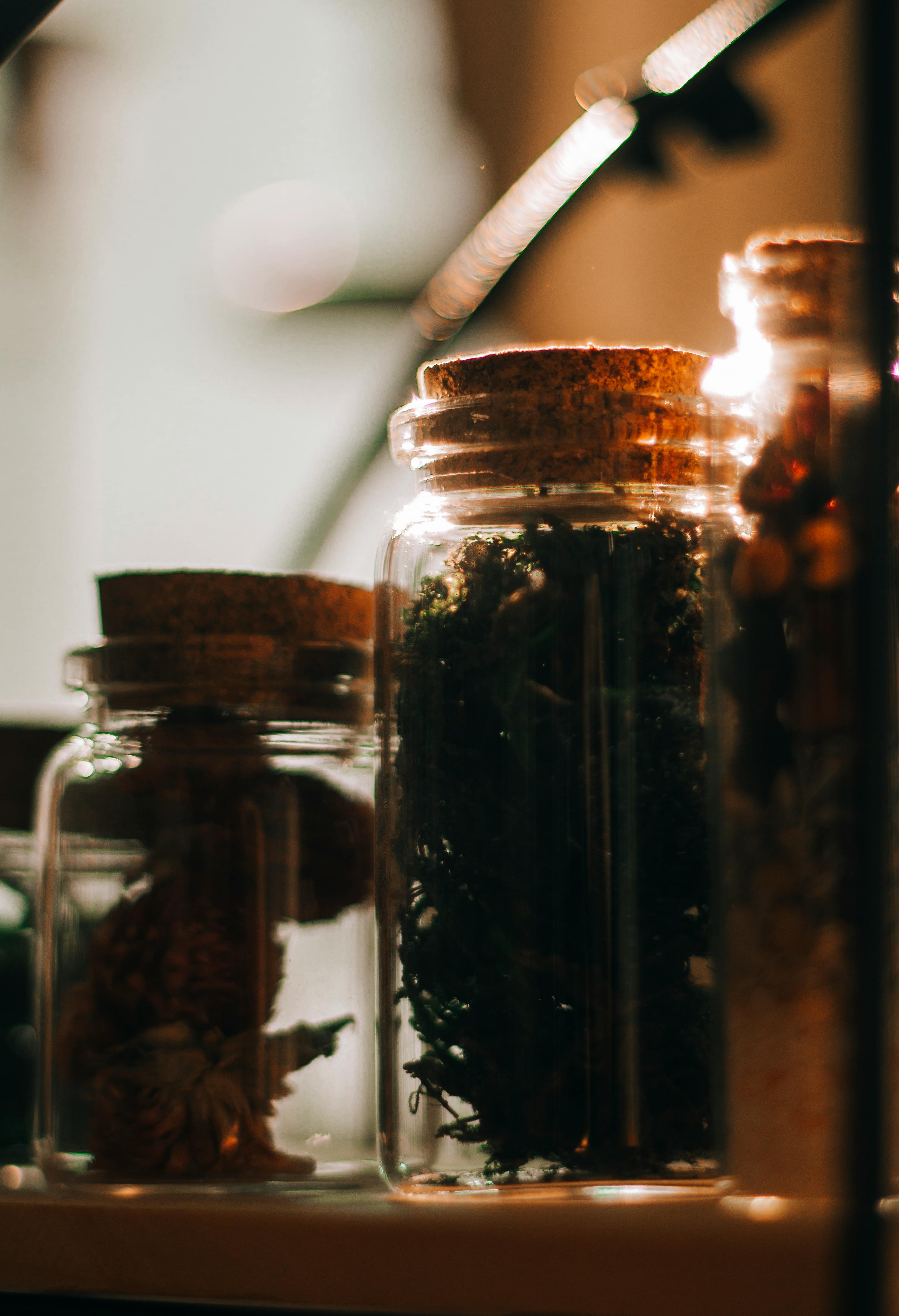 Glass jars of dried herbs with cork lids, warm candlelit shelving