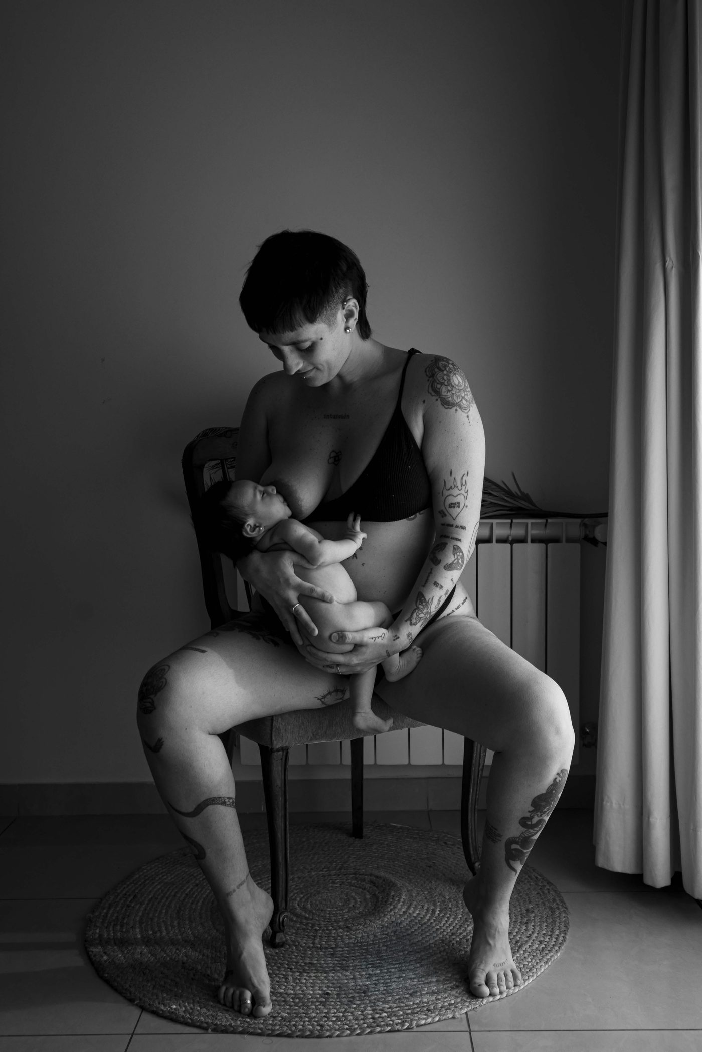 A mother sitting on a wooden chair holding her newborn against her chest